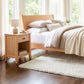 The Andover Modern Nightstand by Maple Corner Woodworks is displayed beside a bed in a bright, minimalist bedroom.