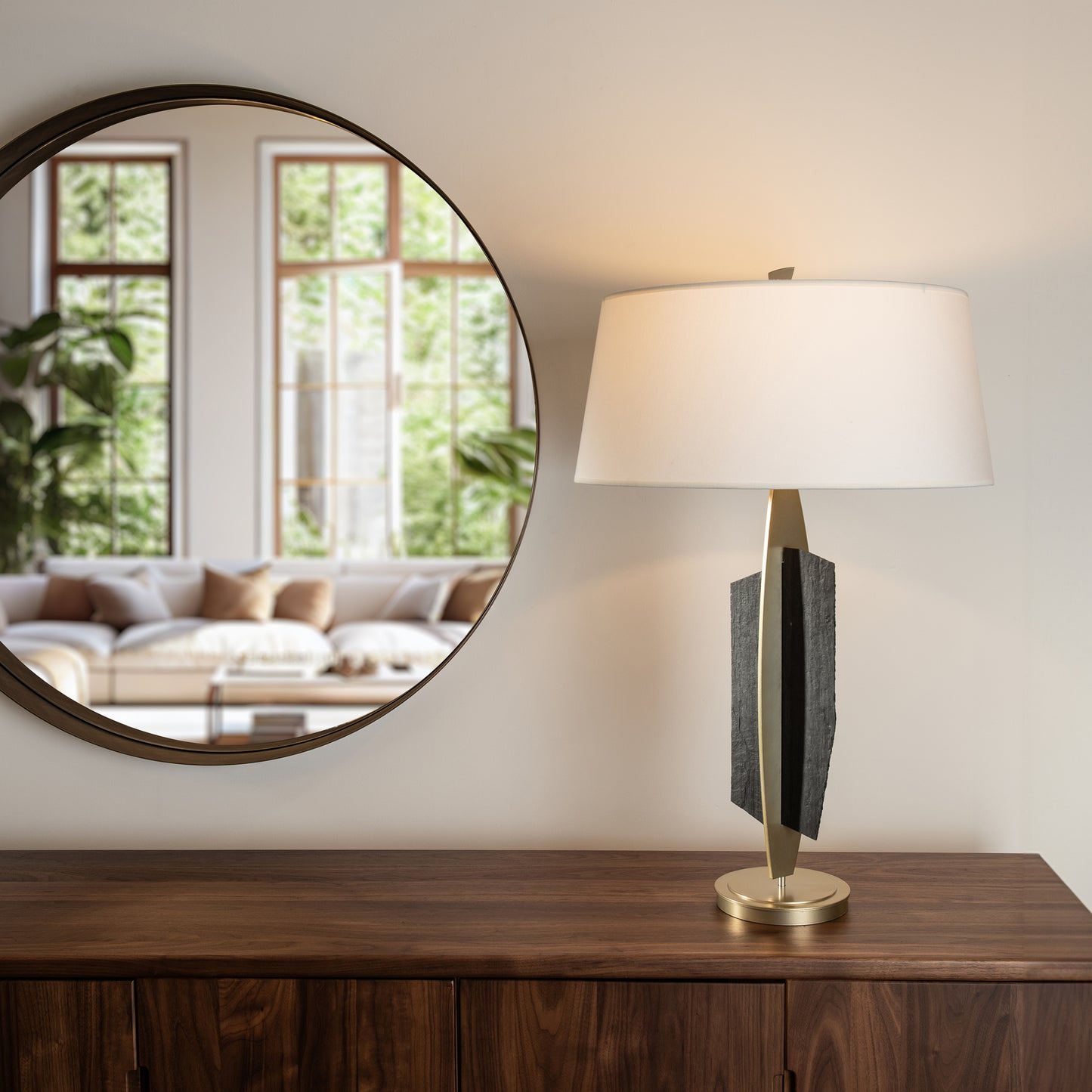 Wooden sideboard with a round mirror and a Cambodia Table Lamp by Hubbardton Forge.