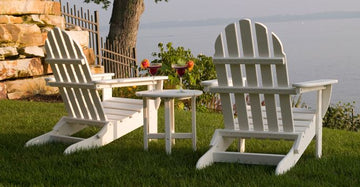 Two white adirondack chairs on a grassy lawn.