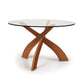 Entwine Round Glass Top Dining Table by Copeland Furniture with sculptural intersecting cherry wood legs and a clear tempered glass top.