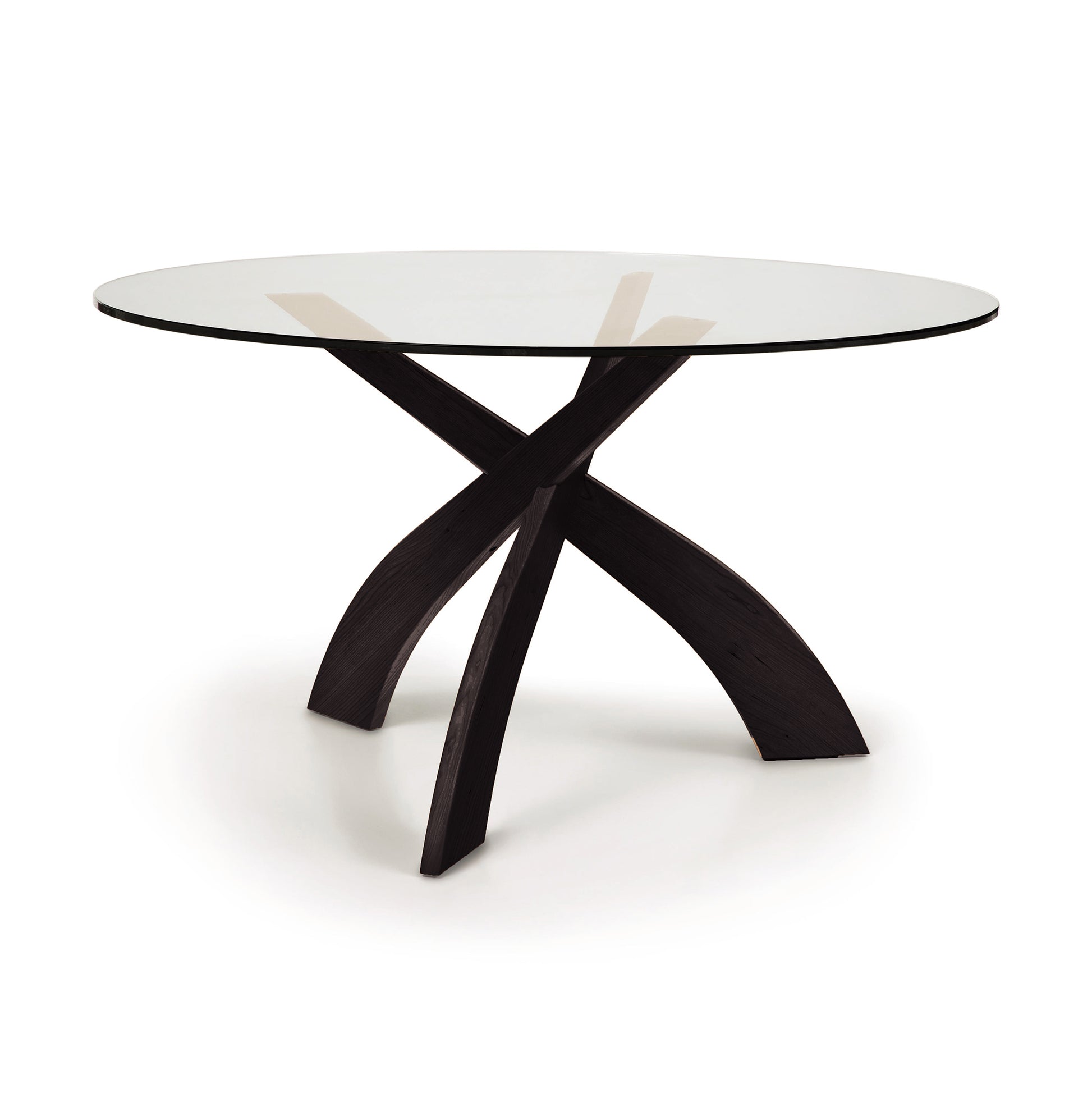 Entwine Round Glass Top Dining Table by Copeland Furniture with curved cherry wood legs and a clear tempered glass top, highlighting artisanal craftsmanship.