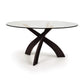 Entwine round dining table by Copeland Furniture featuring a clear tempered glass top and intersecting cherry wood legs, highlighting elegant modern craftsmanship.