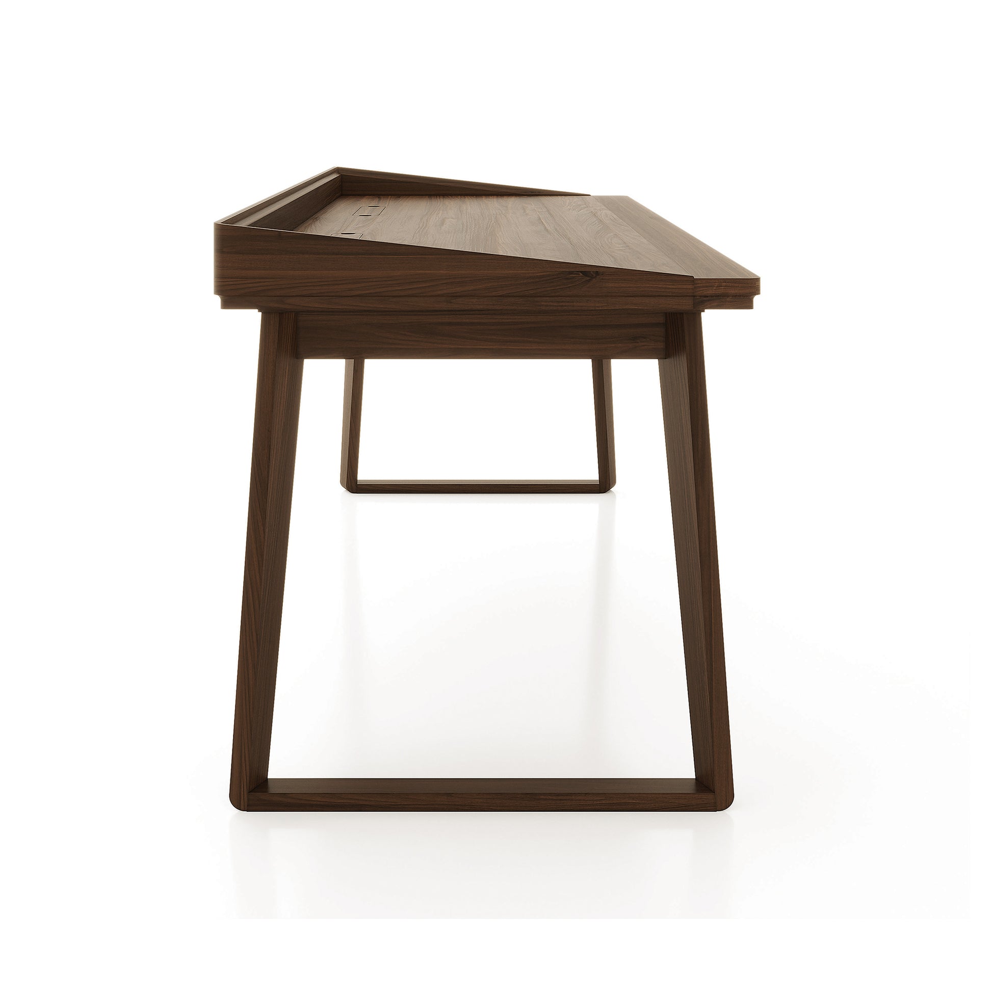 Odin Desk by Copeland Furniture with angled legs and a raised back edge, crafted in America from solid wood, shown in a minimalist setting.