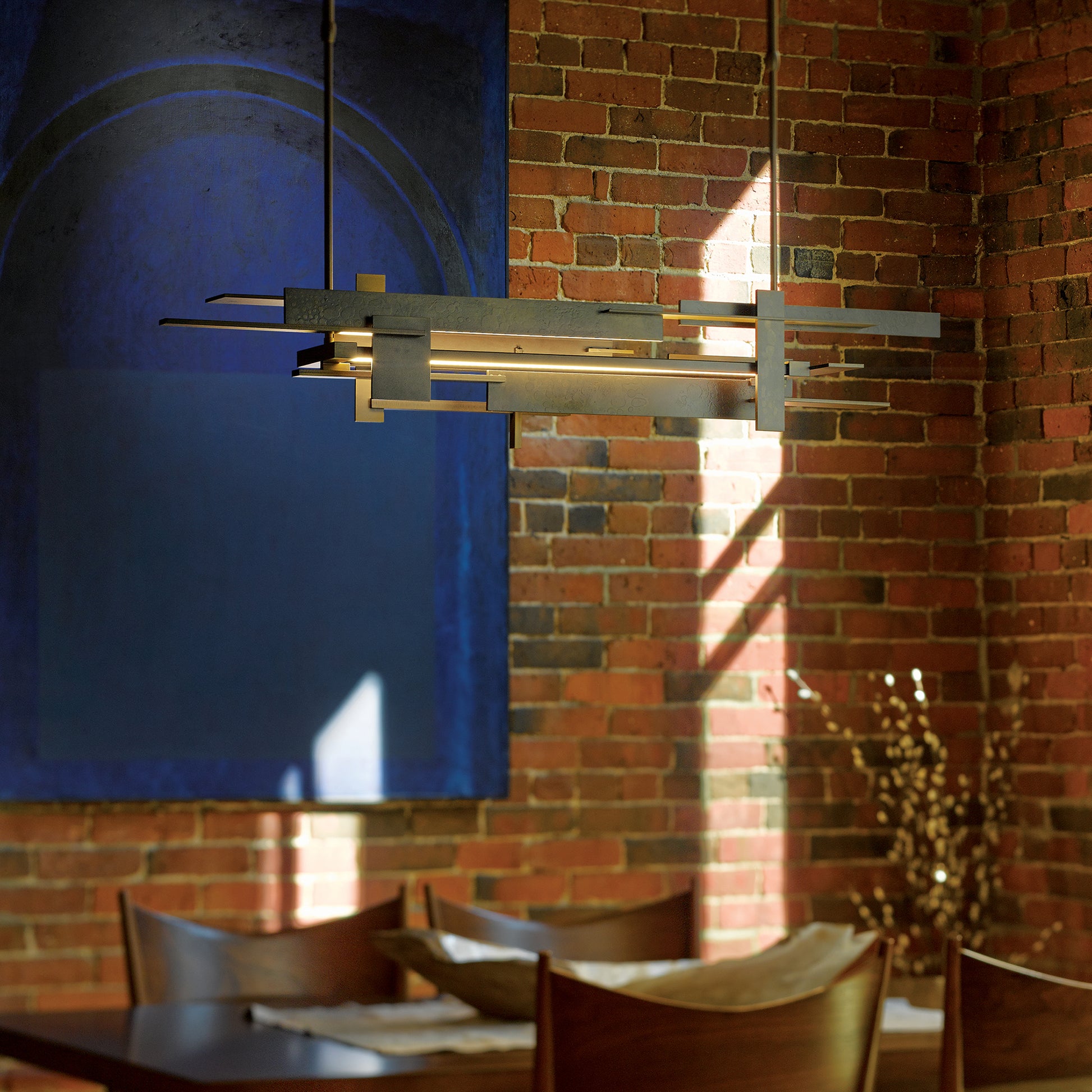 Wooden dining table with brown chairs, complemented by a Hubbardton Forge Planar LED pendant, set against a minimal background.