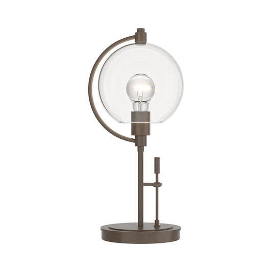 Pluto Table Lamp by Hubbardton Forge with glass shade, dark smoke metal base, and adjustable arm displayed as a floor model.