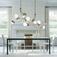 Black modern dining table with sleek white chairs set under elegant Hubbardton Forge Sprig Pendant lighting.