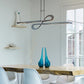 Elegant wooden dining table with white chairs, highlighted by a Hubbardton Forge Switchback Pendant above; minimal decor in view.
