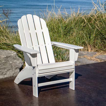 A white adirondack chair in front of the ocean.