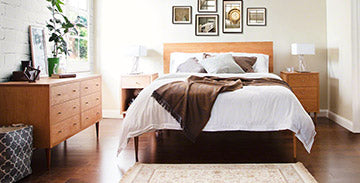 Wooden bed frame with white bedding, accompanied by two bedside tables and a matching dresser.