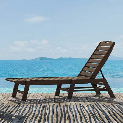 A lounge chair on a wooden deck next to the ocean.