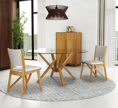A modern dining room features a glass-top round table with a geometric wooden base, accompanied by two wooden chairs with upholstered seats. A wooden cabinet stands against a wall with vertical wood panels. A potted plant is visible in the corner.