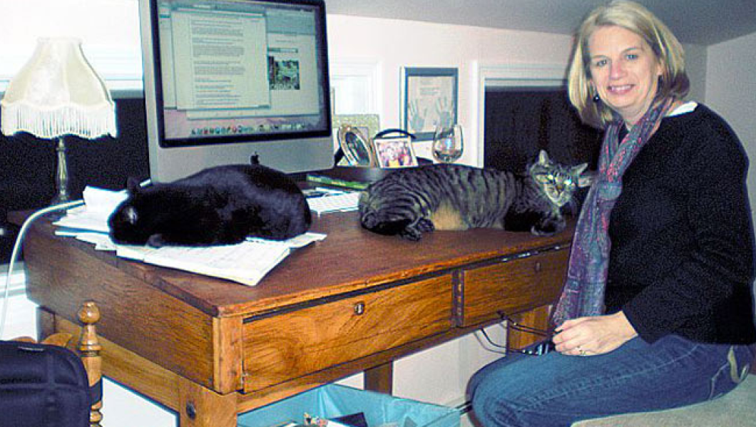 A woman sitting at a desk with two cats.