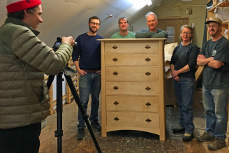 A group of people standing in front of a wooden dresser.