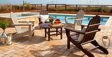 Adirondack chairs on a brick patio near a swimming pool.
