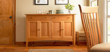 A wooden dresser in a room with a chair and a picture.